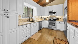 A kitchen with white cabinets, a stone backsplash, stainless steel appliances, and a wooden ceiling. - Pine View Escape w/ Hot Tub (Big Bear)