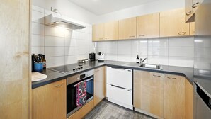 A modern kitchen with wooden cabinets, a black countertop, a built-in oven, and a stainless steel sink.
