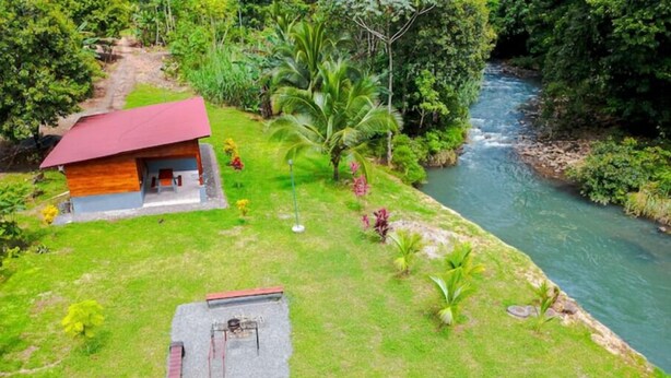 A house with a red roof, a small porch, and a patio area with a table and chairs. - Private River - Nature Cabin Near La Fortuna (La Fortuna,)