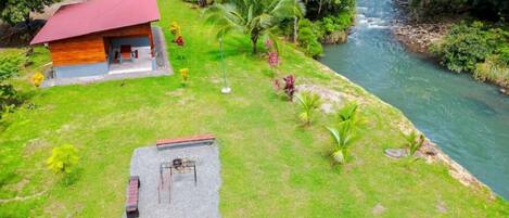 A small house with a red roof, a grassy yard, and a river.