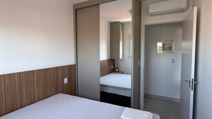 A hotel room with a bed, a mirror, an air conditioning unit, and a door leading to another room. - Red  (Bauru)