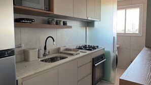 A modern kitchen with a built-in microwave, stainless steel appliances, and a window providing natural light. - Red  (Bauru)