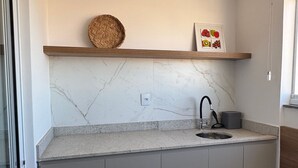 A compact kitchen with a marble backsplash, a wooden shelf, a sink, and a small window. - Red  (Bauru)