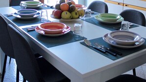 Ruokailutila, jossa on neljälle katettu ruokapöytä, hedelmäkulho ja taustalla keittiö.