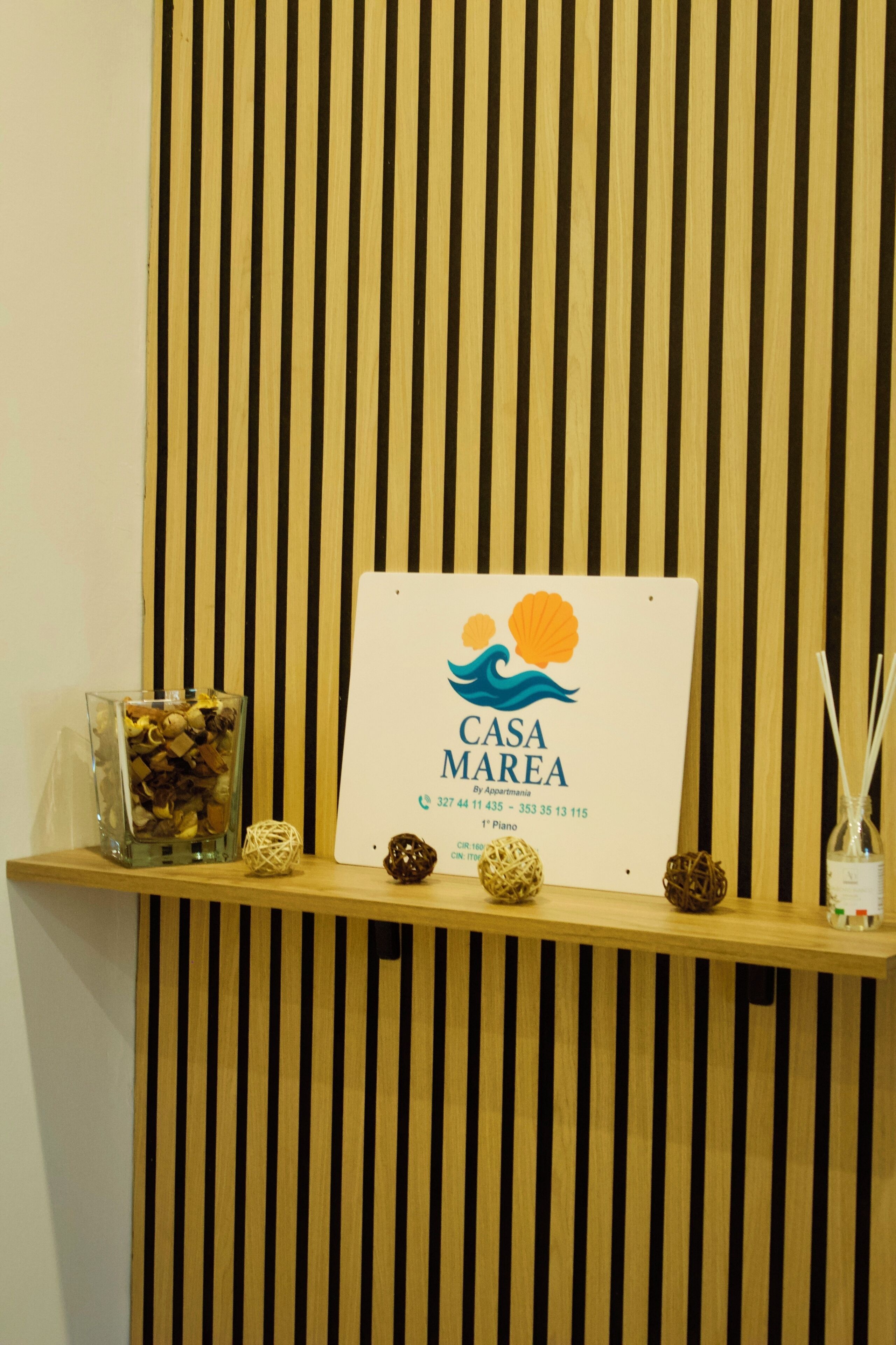 A reception desk with a sign for Casa Marea, a glass container with decorative items, and a small bottle with reed sticks.