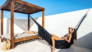 A hammock attached to a wooden structure with a bed and a bag on the floor.