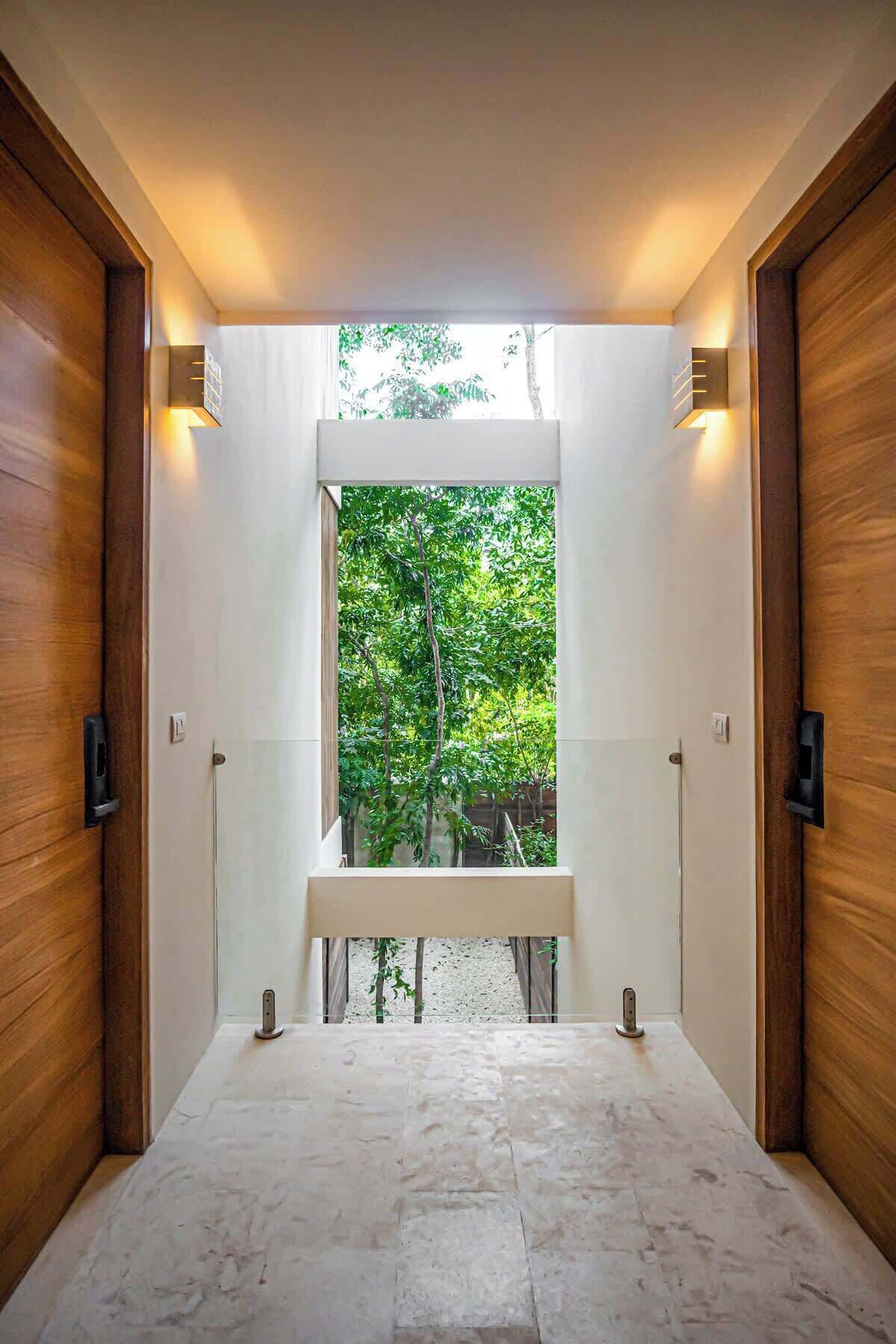 A hallway with a bench, wooden doors, and a view of greenery outside.