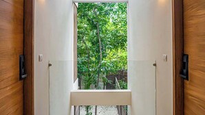 A hallway with a bench, wooden doors, and a view of greenery outside.