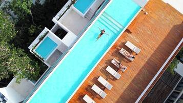 An aerial view of a modern hotel with a rooftop swimming pool, multiple lounge areas, and a wooden deck.
