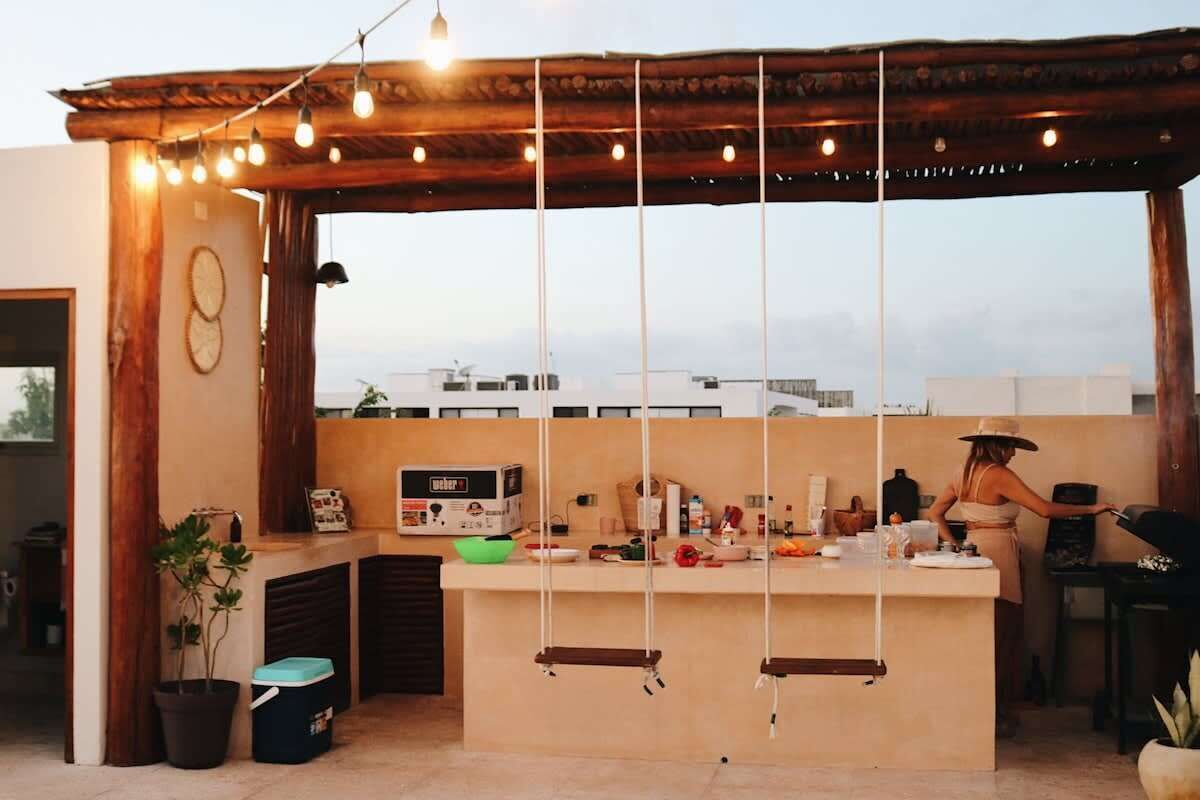 A rooftop bar with a wooden pergola, string lights, a bar counter, and a view of buildings in the background.