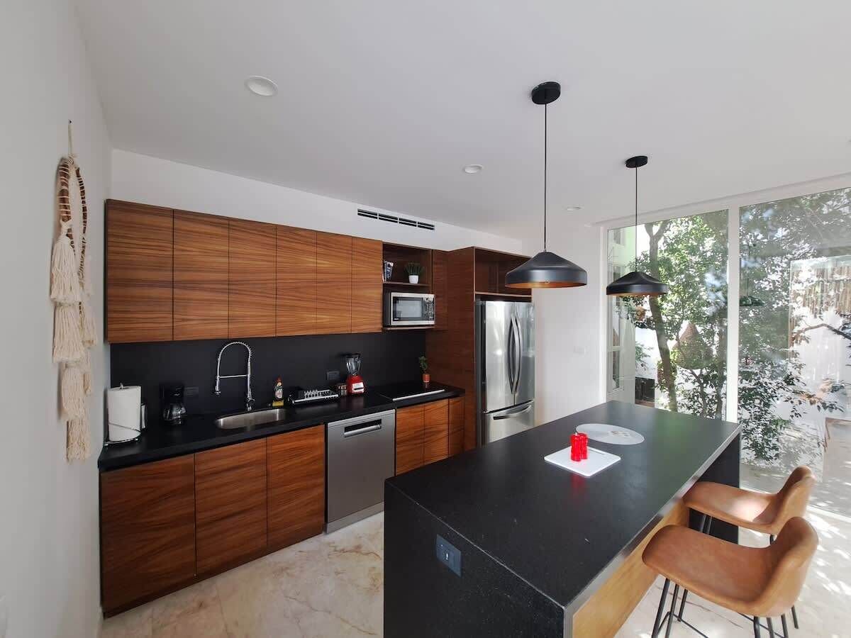 A modern kitchen with wooden cabinets, a black countertop, stainless steel appliances, and a large island with bar stools.