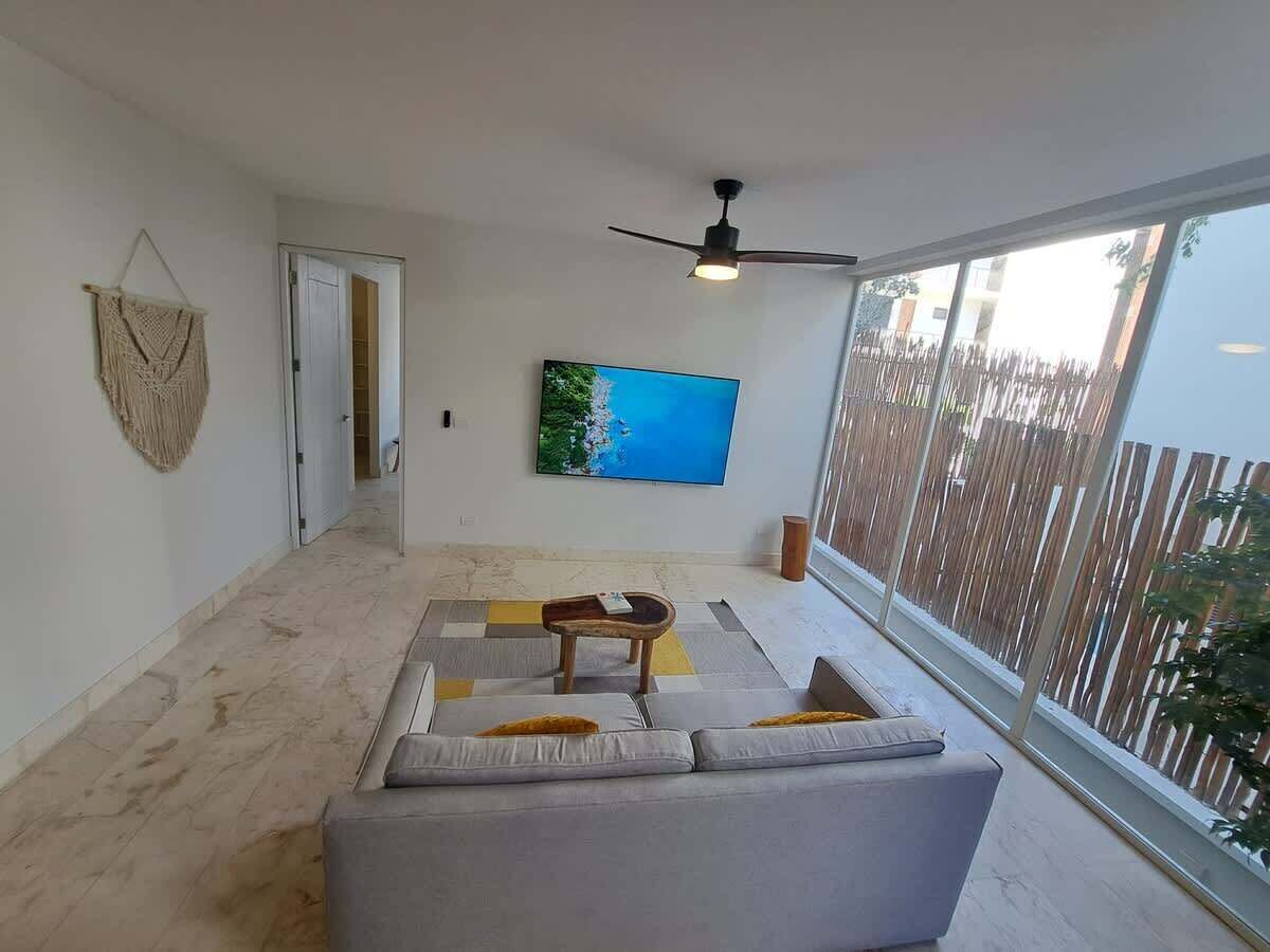 A living room with a sofa, a coffee table, a television, and a ceiling fan.