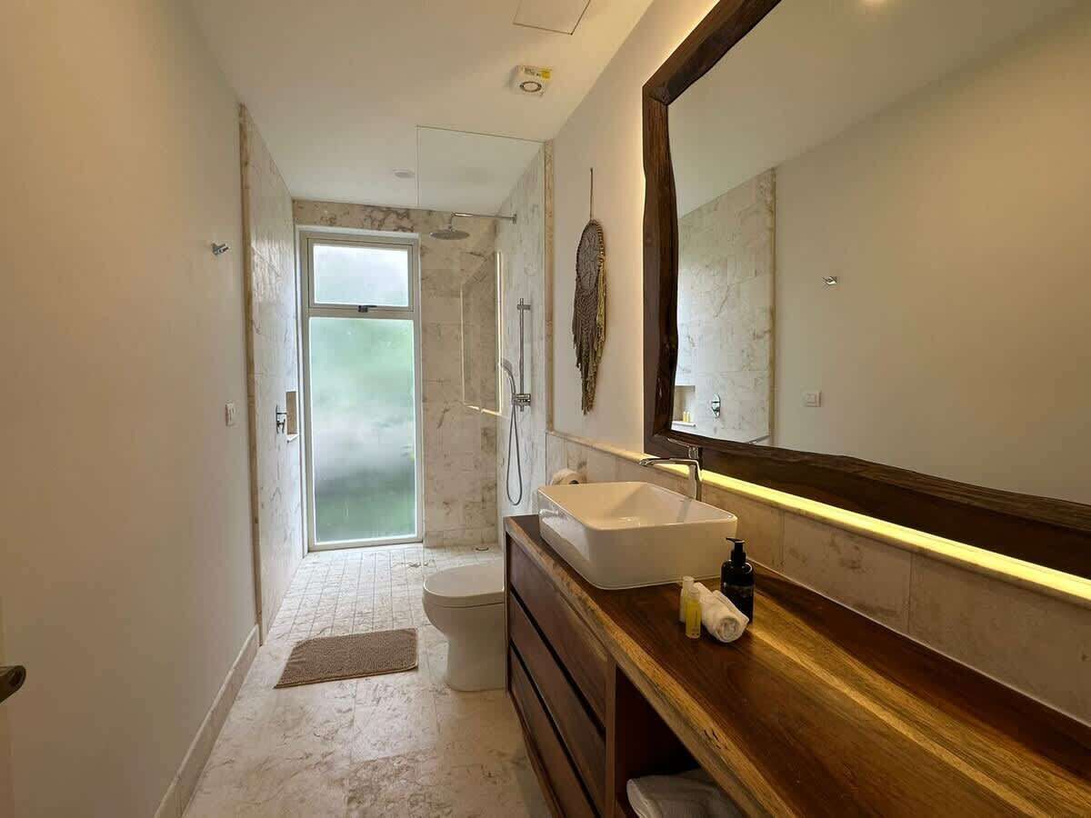 A modern bathroom with a large mirror, a wooden vanity, a sink, and a shower area.