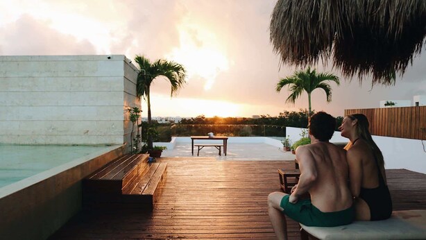 A couple sitting on a wooden deck overlooking a swimming pool, with a sunset in the background. - 3 Bedrooms Penthouse-Private Pool-Free parking (Tulum)