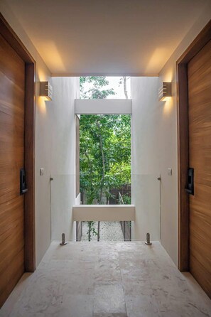 A modern hallway with a bench, wooden doors, and a view of greenery outside.
