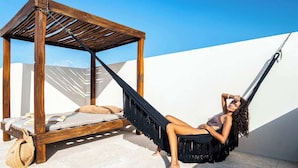 Een houten bed met een hangmat bevestigd aan een houten frame, een klein tafeltje en een tas op de vloer.