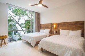 A bedroom with two beds, a ceiling fan, and a large window with a view of greenery. - Tulum Oasis: 3BR Penthouse with Private Pool (Tulum)