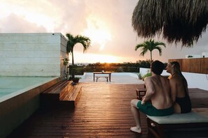 A couple sitting on a wooden deck overlooking a pool with a sunset view. - Tulum Oasis: 3BR Penthouse with Private Pool (Tulum)