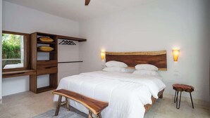 A bedroom with a large bed, a wooden bench, a desk with shelves, and a ceiling fan.