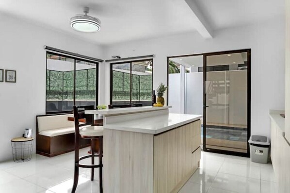 A modern kitchen with a central island, large windows, and a sliding glass door leading to a balcony.