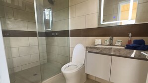 Un baño moderno con ducha de vidrio, inodoro y tocador con espejo.