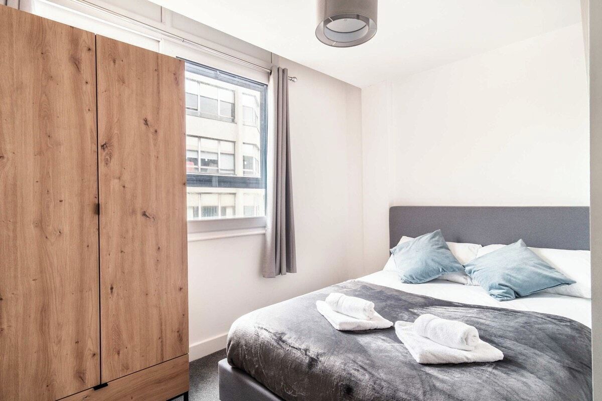 Un dormitorio con cama, armario, ventana con cortinas y vista a edificios.