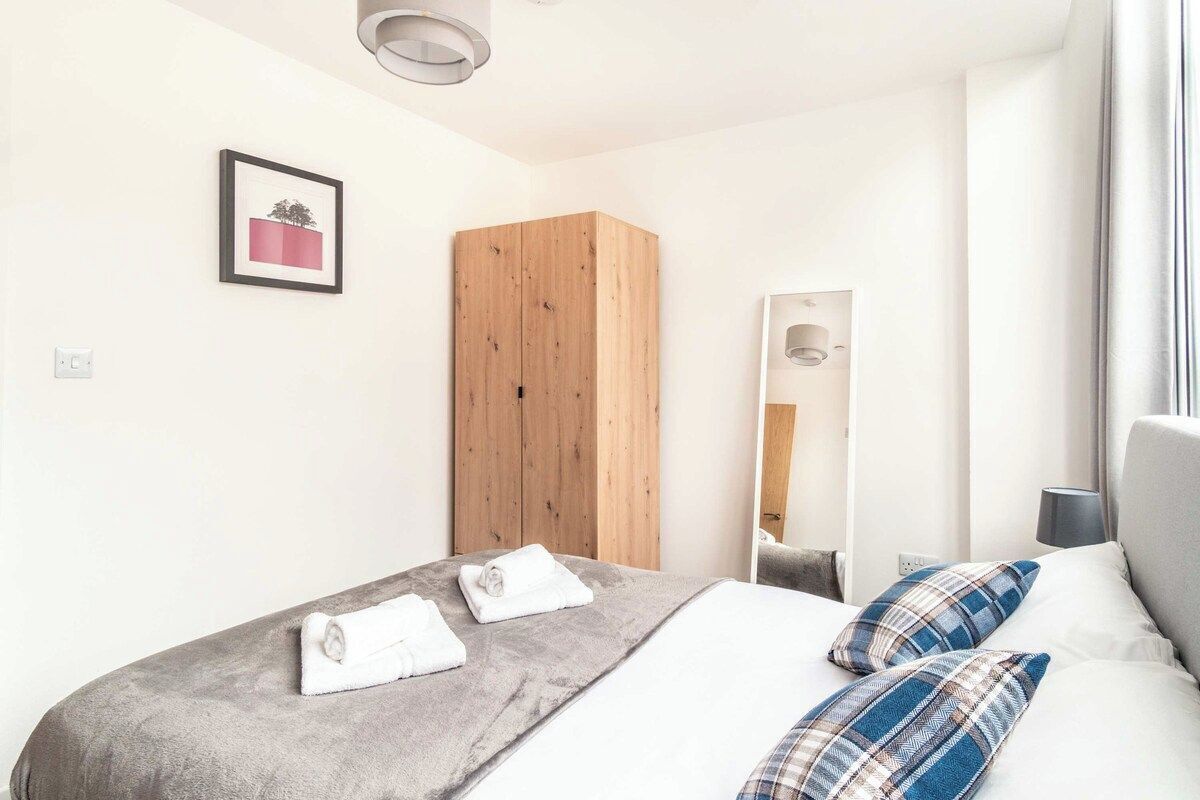 A hotel room with a bed, a wooden wardrobe, a framed picture on the wall, and a window with curtains.