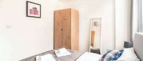 A hotel room with a bed, a wooden wardrobe, a framed picture on the wall, and a window with curtains.