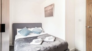 A hotel room with a bed, a bedside table, a wall-mounted TV, and a door.