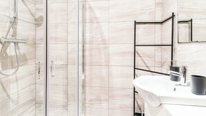 A modern bathroom with a glass shower enclosure, a white sink with a black cup, and a black towel rack.