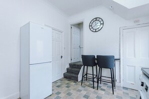 A compact kitchen with white cabinetry, a clock on the wall, and a small bar stool.