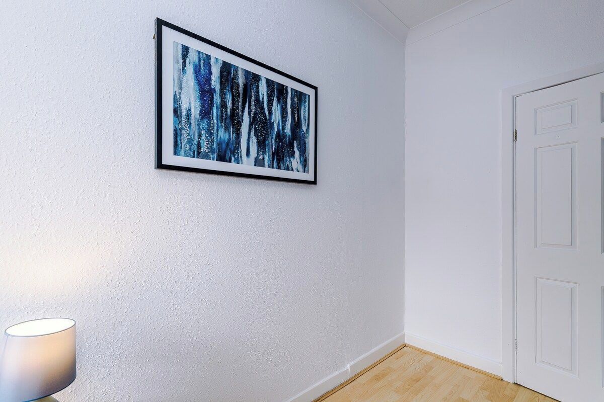 A room with a white door, a framed abstract painting on the wall, and a lamp on the floor.