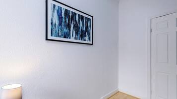 A room with a white door, a framed abstract painting on the wall, and a lamp on the floor.