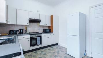 A compact kitchen with white cabinets, a microwave, a stove, and a refrigerator.