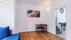 A room with a wooden floor, a blue sofa, a dining table with chairs, a wall-mounted abstract painting, and a door leading to another room. - Preston PR2 Home | Ashton-on-Ribble | Parking (Lancashire)