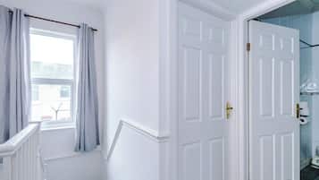 A white door with a brass handle, a window with light blue curtains, and a white radiator.