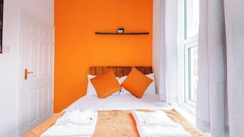 A hotel room with a bed, pillows, a shelf with a small item, and a window with curtains.
