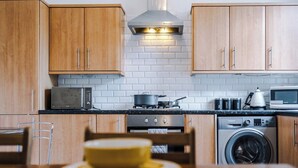 A kitchen with wooden cabinets, a microwave, a stove, a washing machine, and a dining table with a yellow plate. - 15%OFF|Stay7PayLess|Business|Parking|WiFi|Sleeps7 (Lancashire)