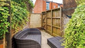 A small outdoor seating area with wicker furniture, a wooden gate, and a brick wall partially covered with ivy. - 15%OFF|Stay7PayLess|Business|Parking|WiFi|Sleeps7 (Lancashire)