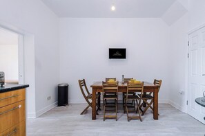 Un comedor con una mesa y sillas de madera, un cubo de basura negro y un televisor montado en la pared.