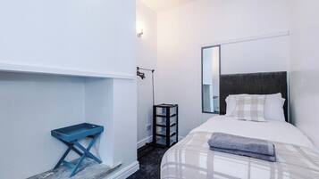 A hotel room with a bed, a bedside table, a mirror, and a small shelf.