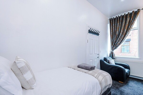 Un dormitorio con cama, una silla, una ventana con cortinas y una puerta.