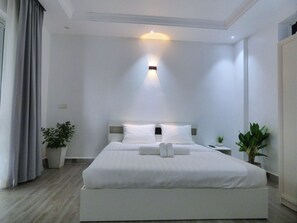 A modern hotel room with a large bed, a bedside table, and two potted plants.