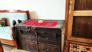 A vintage trunk with metal latches and a red cloth on top, placed next to a wooden door and a cushioned bench with colorful pillows. - Silver Hill Guesthouse (Gjirokastër)