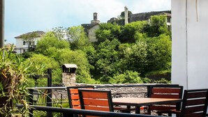 An outdoor patio with stone tables and chairs, overlooking a lush green hillside with historic buildings. - Silver Hill Guesthouse (Gjirokastër)