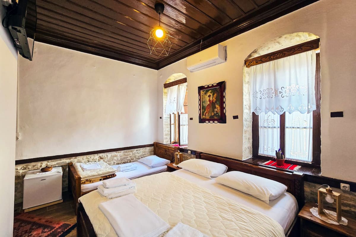 A room with two beds, a wooden ceiling, and a window with curtains.