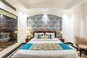 Une chambre d’hôtel avec un grand lit, un papier peint à motifs floraux, un mur en marbre et un fauteuil en cuir.