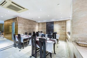Een moderne eetruimte met meerdere tafels en stoelen, een marmeren wand en een plafond met inbouwverlichting.