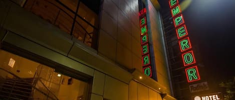 Un hotel con un letrero de neón que dice "EMPEROR" y un cartel que indica "HOTEL EMPEROR PALMS BY ALAYASTAYS".