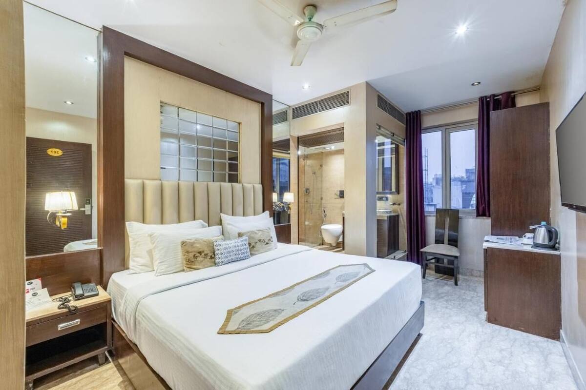 Quarto de hotel com uma cama grande, uma escrivaninha com cadeira, um espelho e vista para a cidade pela janela.